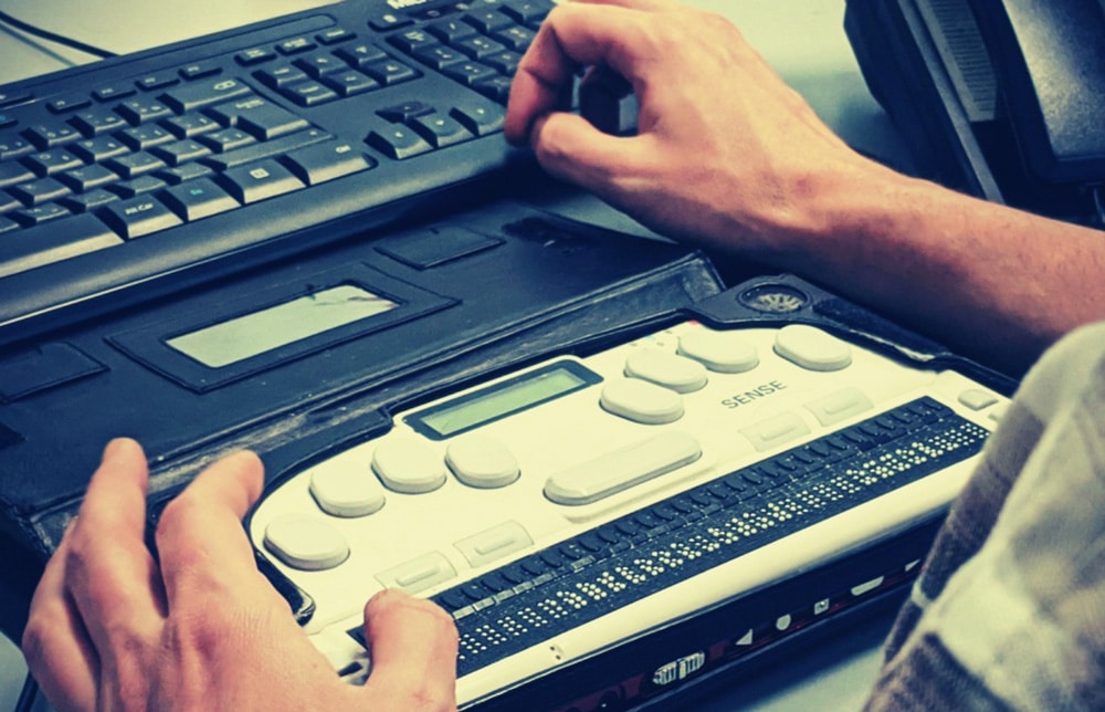 Person using a refreshable Braille display to access digital content on a computer.
